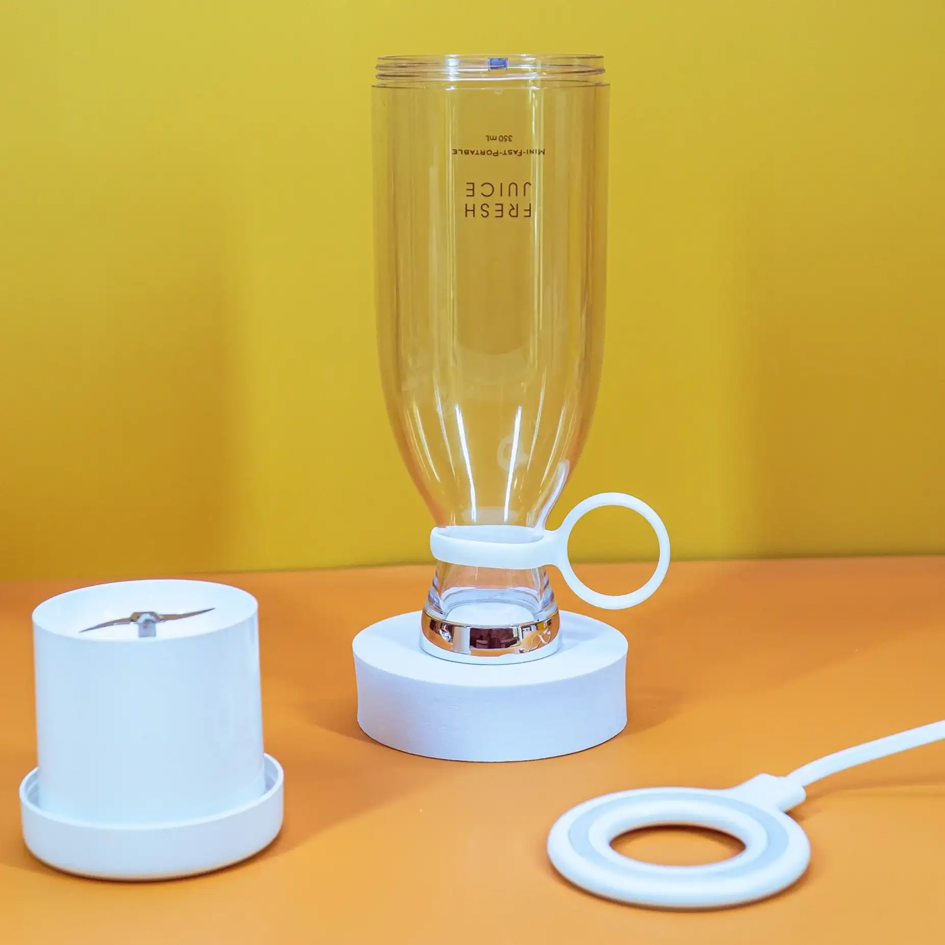 An upside down white Fresh Juice blender, surrounded by a charger and blender base, in front of an orange and yellow background.