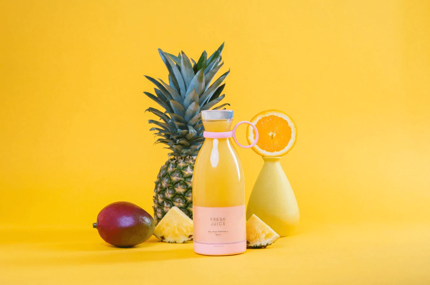 A yellow Fresh Juice blender filled with yellow juice and surrounded by pineapples and oranges on a yellow background.