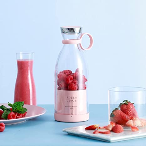 A pink Fresh Juice portable blender filled with raspberries surrounded by a cup filled with strawberries on a blue background.